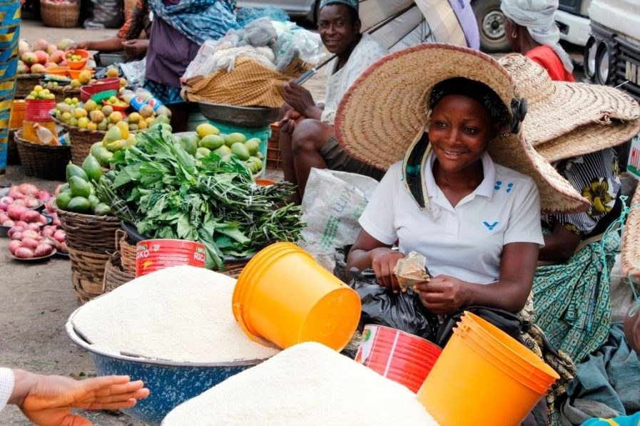 A trader behind bowls of rice and fresh produce